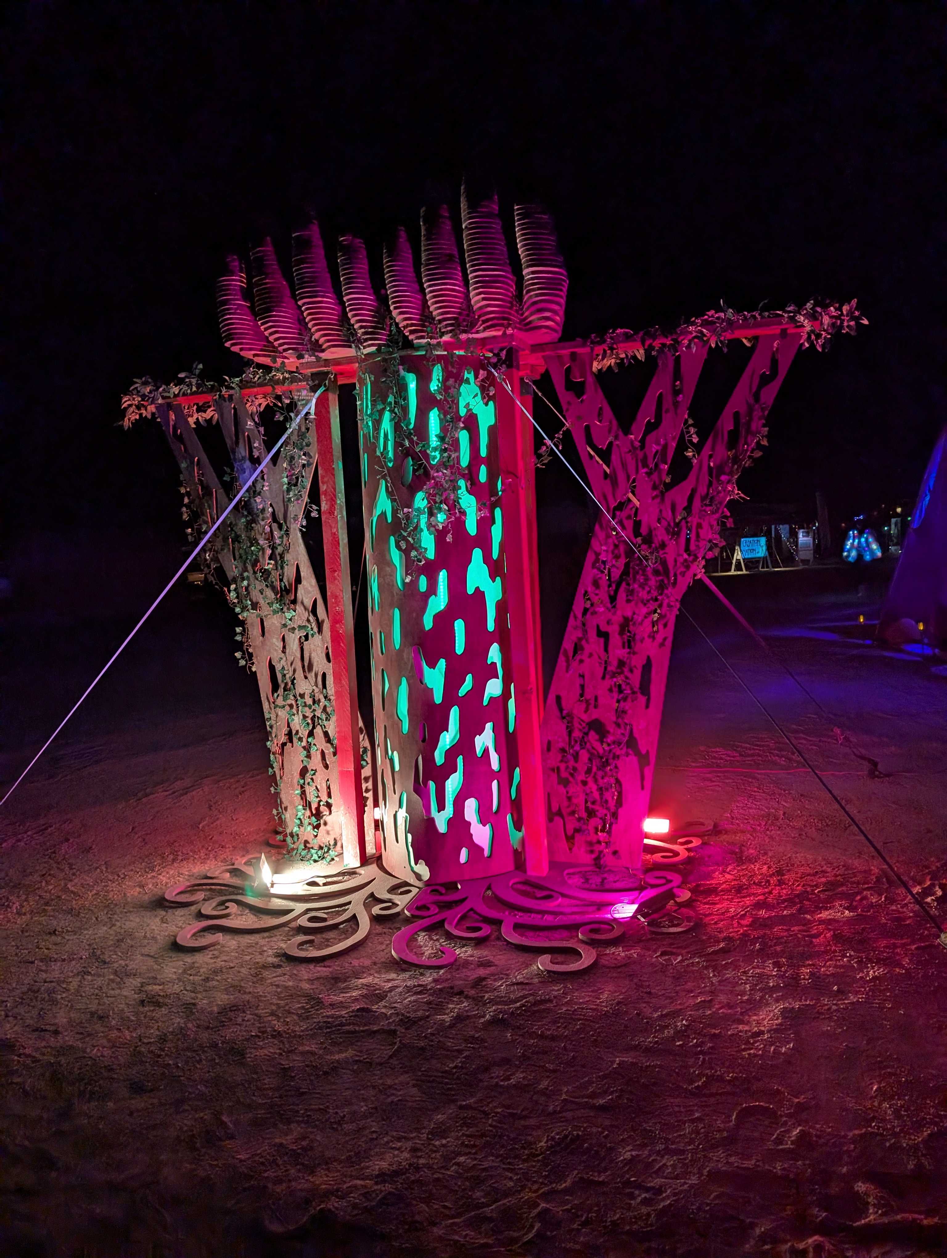 Lover's Tree installation at night, illuminated with vibrant pink and turquoise lights